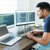 Side view of attractive Hispanic software developer programming using computer while working from home