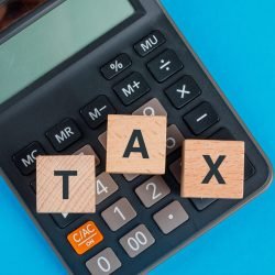 Tax planning concept with wooden cubes on calculator on blue background flat lay.